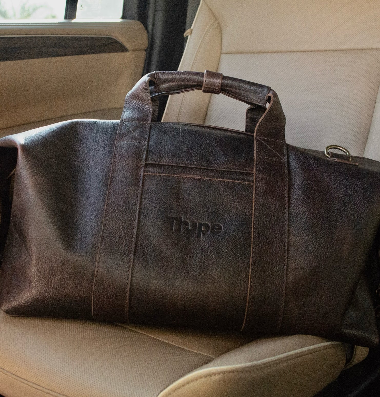 Bolsa duffle negra Thupe con asas superiores y logo grabado colocada en asiento de automóvil, estilo viaje elegante.