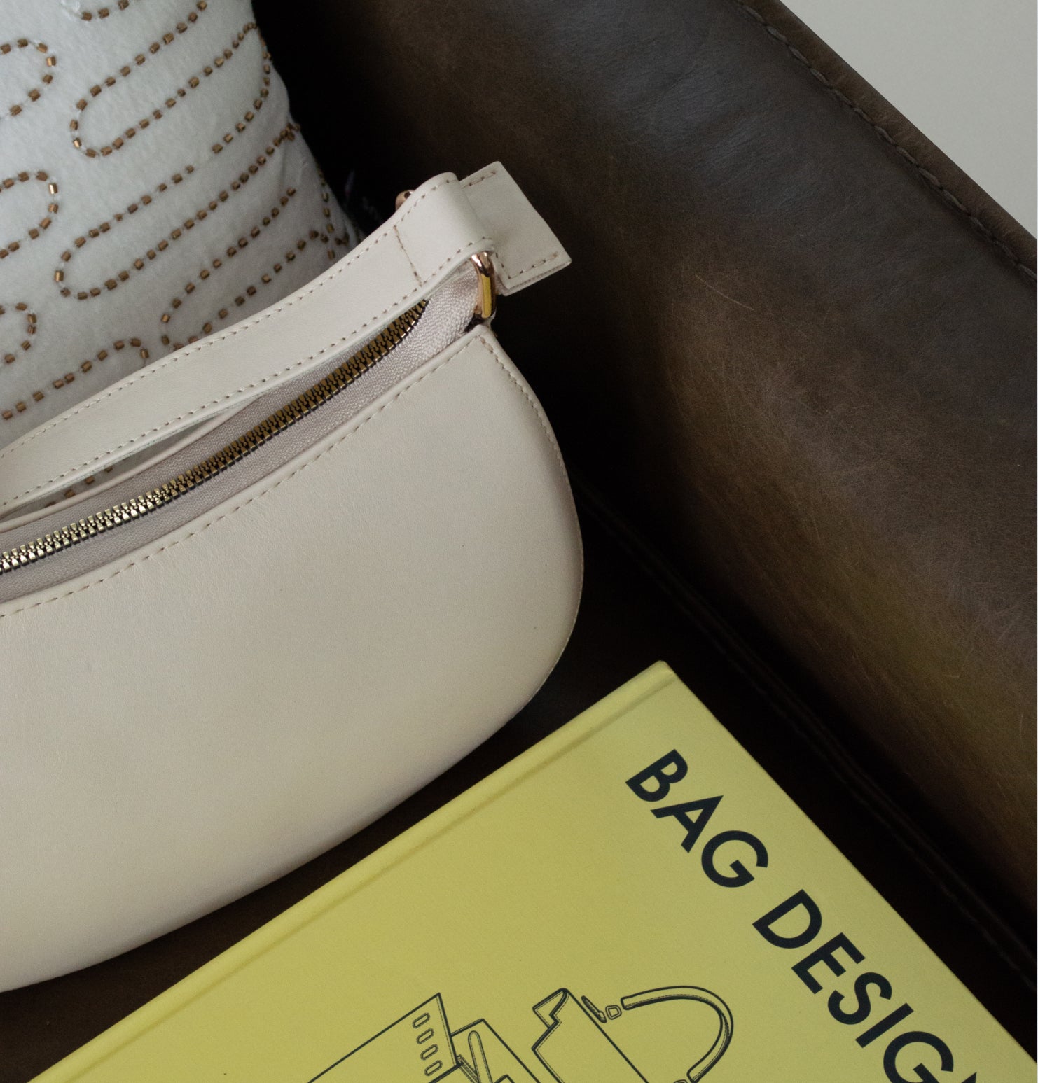 Bolso Thupe beige tipo shoulder bag con silueta curva y herrajes dorados en estilo minimalista contemporáneo.