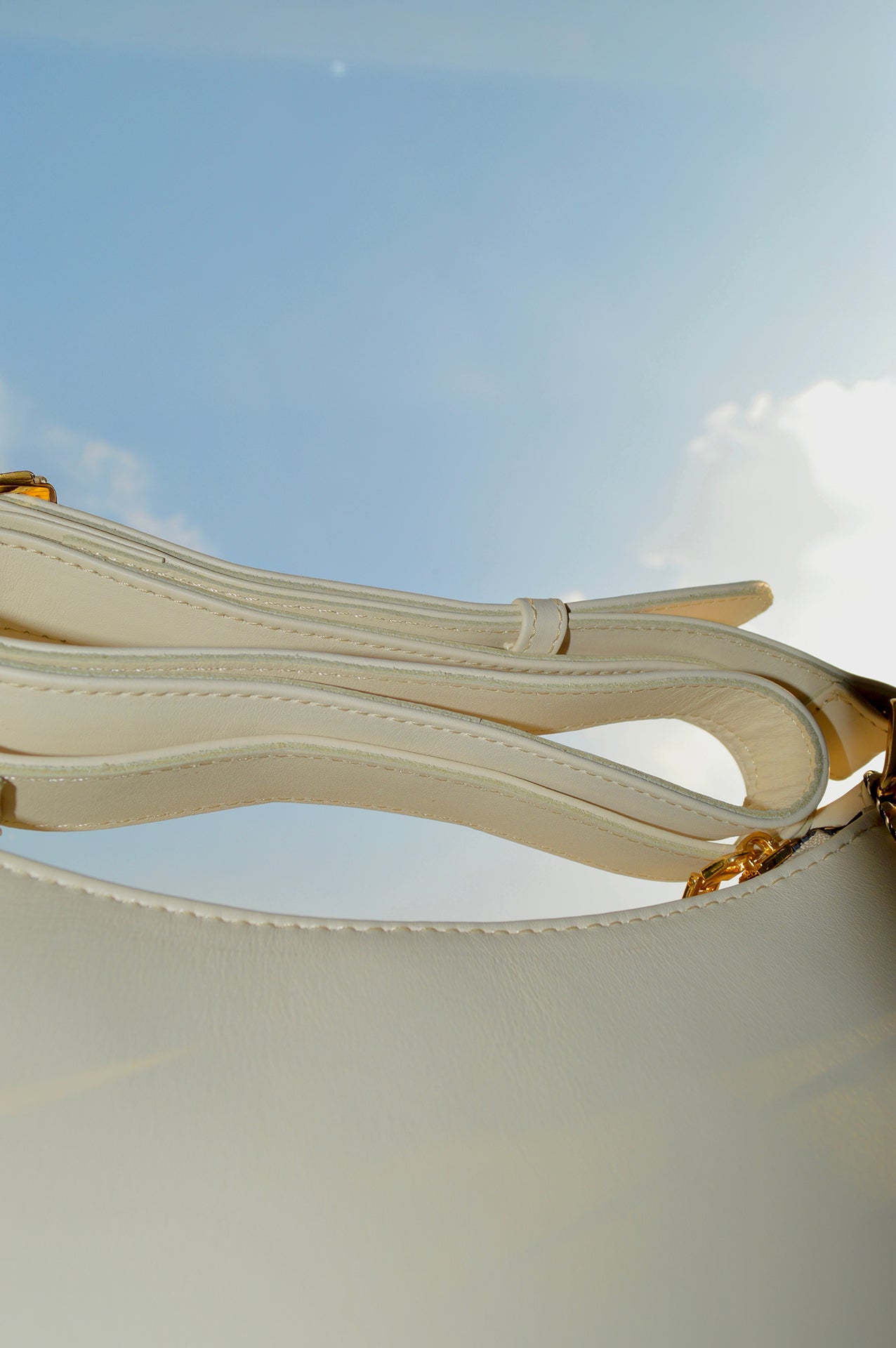 Detalle de asa y herrajes dorados en bolso Thupe beige minimalista con costuras visibles.